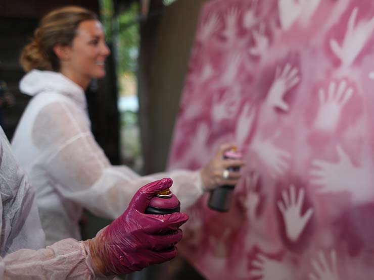 Foto von gemeinsamer Arbeit bei einem Streetart Workshop mit Teambuilding Elementen. Mit Sprühdosen und Händen wird eine Leinwand gestaltet.